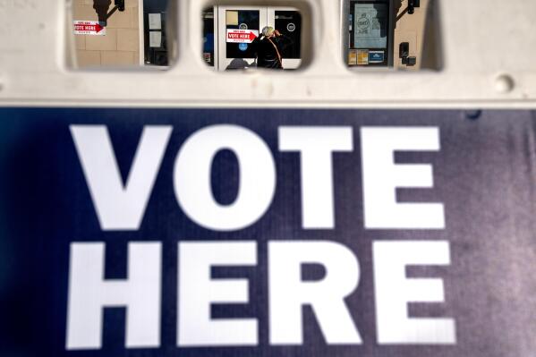 A woman is seen through a "vote here" sign, as she enters a polling site to vote in the midterm elections, Tuesday, Nov. 8, 2022, in Washington. (AP Photo/Jacquelyn Martin)