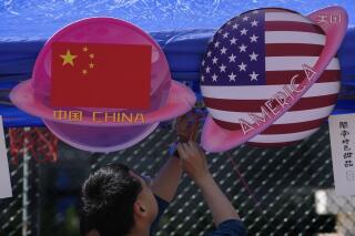 A vendor sets up foods and beverages at a booth displaying planets shaped of China and American flags during a Spring Carnival in Beijing on May 13, 2023. Hong Kong's leader on Tuesday, May 16 said the sentencing on spying charges of a U.S. citizen in China, who was also a permanent resident of the semi-autonomous city, illustrated that the territory should "stay vigilant to national security risks hidden in society." (AP Photo/Andy Wong)
