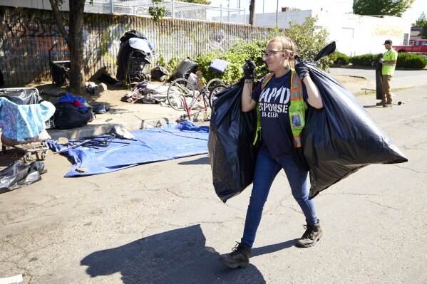 Amber Nastasia from Rapid Response Bio Cleanup cleans a homeless camp in Portland, Ore., Thursday, July 27, 2023. Cities across the U.S. are struggling with and cracking down on tent encampments as the number of homeless people grows, largely due to a lack of affordable housing. Homeless people and their advocates say sweeps are cruel and costly, and there aren't enough homes or beds for everyone. (AP Photo/Craig Mitchelldyer)
