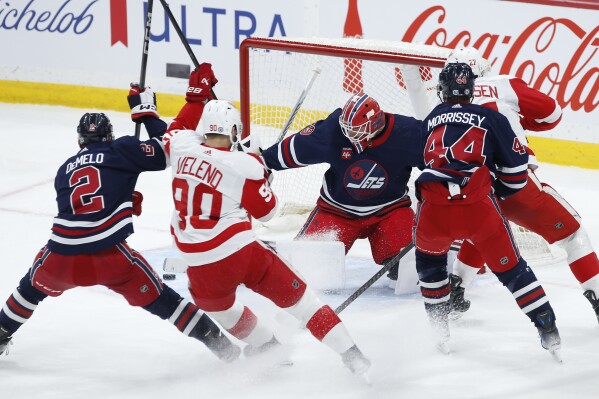 Winnipeg Jets goaltender Laurent Brossoit (39) makes a save against Detroit Red Wings' Michael Rasmussen, back right, during the first period of an NHL hockey game Wednesday, Dec. 20, 2023, in Winnipeg, Manitoba. (John Woods/The Canadian Press via AP)