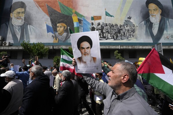 Iranian worshippers walk past a mural showing the late revolutionary founder Ayatollah Khomeini, right, Supreme Leader Ayatollah Ali Khamenei, left, and Basij paramilitary force, as they hold posters of Ayatollah Khomeini and Iranian and Palestinian flags in an anti-Israeli gathering after Friday prayers in Tehran, Iran, Friday, April 19, 2024. (AP Photo/Vahid Salemi)