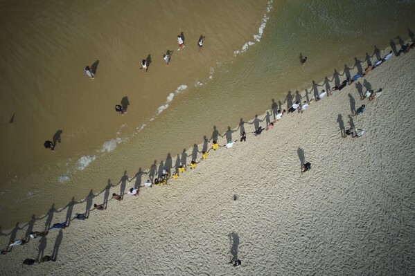 Un grupo de personas se toman de la mano a lo largo de la playa de Sao Conrado para un abrazo grupal simbólico al mar en el Día Mundial de los Océanos, el 8 de junio de 2025, en Río de Janeiro. (AP Foto/Silvia Izquierdo)