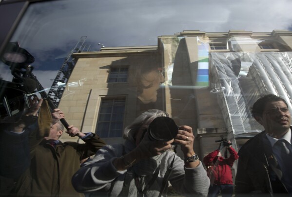 FILE - Journalists, including Associated Press photographer Anja Niedringhaus, reflected in the window at lower center, surround the car of Bouthaina Shaaban, advisor to Syrian President Assad, as she leaves after meeting with the Syrian opposition at the United Nations headquarters in Geneva, Switzerland, Jan. 27, 2014. On April 4, 2014, outside a heavily guarded government compound in eastern Afghanistan, Niedringhaus was killed by an Afghan police officer as she sat in her car. She was 48 years old. (AP Photo/Anja Niedringhaus, File)