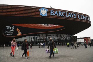 FILE - In this March 12, 2020, file photo, pedestrians walk past the Barclays Center, which is home to the Brooklyn Nets, in the Brooklyn borough of New York. The Nets announced on Tuesday, March 17, 2020, that four players have tested positive for the new coronavirus, bringing the total to seven known players in the NBA. (AP Photo/John Minchillo, File)