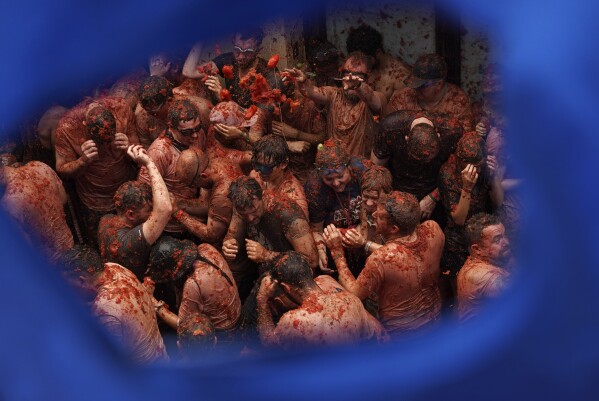 Revellers throw tomatoes at each other during the annual "Tomatina" tomato fight fiesta, in the village of Bunol near Valencia, Spain, Wednesday, Aug. 30, 2023. Thousands gather in this eastern Spanish town for the annual street tomato battle that leaves the streets and participants drenched in red pulp from 120,000 kilos of tomatoes. (AP Photo/Alberto Saiz)