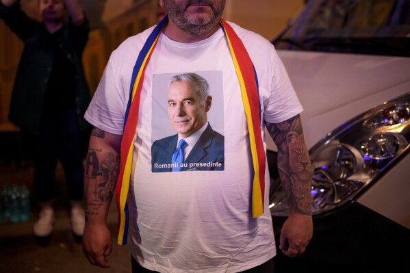 A man wears a t-shirt showing Calin Georgescu, winner of the first round of last year's voided election outside the headquarters of presidential candidate George Simion, after polls closed during the first round of the country's presidential election redo in Bucharest, Romania, Sunday, May 4, 2025. (AP Photo/Andreea Alexandru)