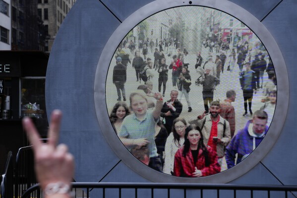 People in both New York and Dublin, Ireland, wave and signal at each other while looking at a livestream view of one another as part of an art installation on the street in New York, Tuesday, May 14, 2024. (AP Photo/Seth Wenig)