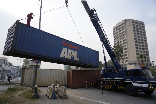 Workers place shipping containers to close a road ahead of a planned rally by supporters of imprisoned former Prime Minister Imran Khan's Pakistan Tehreek-e-Insaf party, in Islamabad, Pakistan, Saturday, Nov. 23, 2024. (AP Photo/Anjum Naveed)