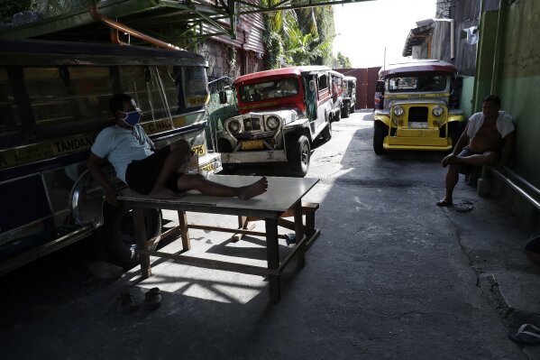 Driver Rey Escanilla, left, sits beside parked jeepneys at the Tandang Sora terminal which have been home for them since a lockdown started three months ago, on Wednesday, June 17, 2020 in Quezon city, Philippines. Espanilla was kicked out of their home after failing to pay their monthly rent during the pandemic. He has now relocated his family to another place but remains jobless. (AP Photo/Aaron Favila)