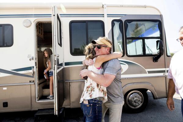 Woody Faircloth hugs Sheri Roen as her family donates their motorhome to EmergencyRV.org on Sunday, Sept. 5, 2021, in Sierra County, Calif. Accompanied by daughter Luna, left, Faircloth delivered it to a Dixie Fire victim later that day, (AP Photo/Noah Berger)