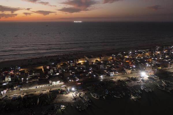 An offshore gas terminal is lit up amid the Atlantic Ocean as houses lay on the beachfront between the sea and the Senegal River, bottom, in Saint Louis, Senegal, Wednesday, Jan. 18, 2023. Fishing has long been the community's lifeblood, but the industry was struggling with climate change and COVID-19. Officials promised the drilling would soon bring thousands of jobs and diversification of the economy. (AP Photo/Leo Correa)
