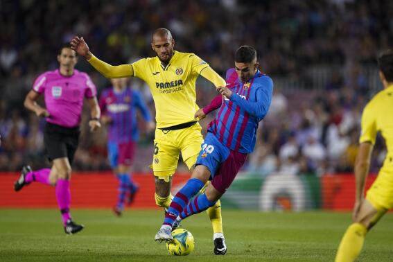 Barcelona's Ferran Torres, right, is challenged by Villarreal's Etienne Capoue during a Spanish La Liga soccer match between Barcelona and Villarreal at the Camp Nou stadium in Barcelona, Spain, Sunday, May 22, 2022. (AP Photo/Joan Mateu Parra)
