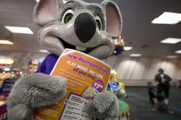 An employee dressed as Chuck E. Cheese holds a flyer advertising new memberships at a location Wednesday, March 13, 2024, in San Diego. (AP Photo/Gregory Bull)