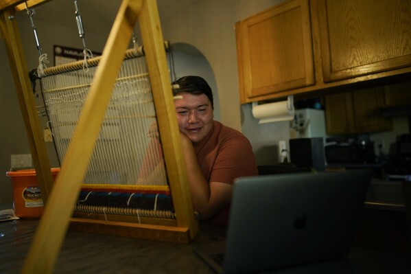 Nikyle Begay smiles while meeting with students via Zoom Thursday, Sept. 7, 2023, on the Navajo Nation in Ganado, Ariz. Begay teaches traditional Navajo weaving online to students as far away as Alaska. (AP Photo/John Locher)