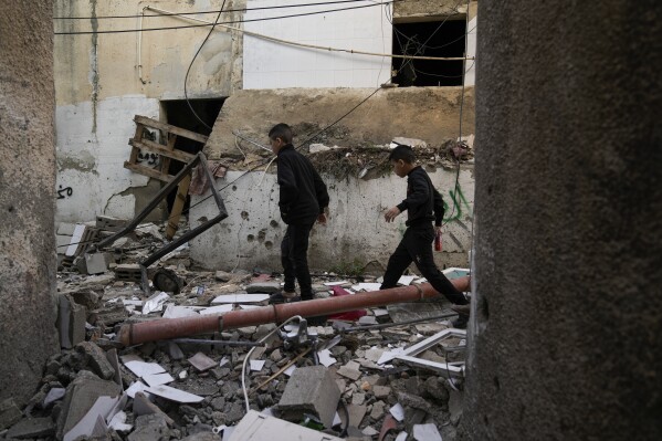 Palestinians walk by a damaged building following an Israeli army operation in Jenin refugee camp, West Bank, Sunday, Nov. 26, 2023. Israeli forces operating in the occupied West Bank killed at least eight Palestinians in a 24-hour period, Palestinian health officials said Sunday. (AP Photo/Majdi Mohammed)