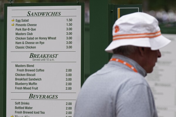 A patron walks past a sign displaying the prices of food items during a practice round in preparation for the Masters golf tournament at Augusta National Golf Club Tuesday, April 9, 2024, in Augusta, Ga. (AP Photo/George Walker IV)