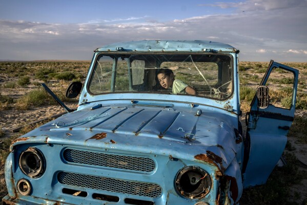 2023年7月2日，星期一，哈萨克斯坦阿拉尔斯克附近的塔图别克村，一个孩子在一辆生锈的破旧汽车里玩耍，汽车行驶在干涸的咸海沿岸。（美联社照片/Ebrahim Noroozi）