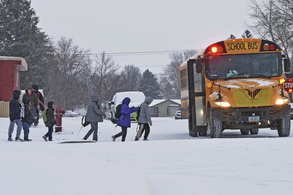 Children in winter coats line up to get into a school bus Thursday, March 21, 2024 in Bismarck, N.D. Parts of Montana, the Dakotas, Minnesota, Illinois and Wisconsin are under winter weather advisories, with snow expected to start falling Thursday in some areas. Minnesota could see a foot of snow over the weekend, and parts of New England could also see 12 to 18 inches (30 to 45 centimeters) in the coming days. (Tom Stromme/The Bismarck Tribune via AP)