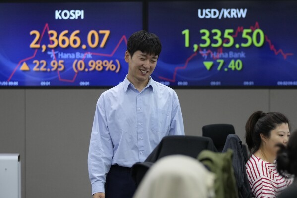 A currency trader passes by the screens showing the Korea Composite Stock Price Index (KOSPI), left, and the foreign exchange rate between U.S. dollar and South Korean won at the foreign exchange dealing room of the KEB Hana Bank headquarters in Seoul, South Korea, Friday, Nov. 3, 2023. (AP Photo/Ahn Young-joon)