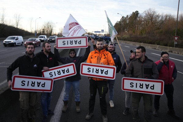 Farmers hold upside down road signs of Paris on a blocked highway, Wednesday, Jan. 31, 2024 in Chilly-Mazarin, south of Paris. Farmers blocked more traffic arteries across Belgium, France and Italy on Wednesday, as they sought to disrupt trade at major ports and other economic lifelines. They also moved closer to Brussels on the eve of a major European Union summit, in a continued push for better prices for their produce and less bureaucracy in their work. (AP Photo/Christophe Ena)