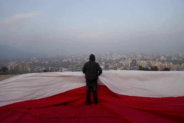 A demonstrator stands on a giant Chilean flag before a rally against the proposed new Constitution in Santiago, Chile, Thursday, Sept. 1, 2022. Chileans have until the Sept. 4 plebiscite to study the new draft and decide if it will replace the current Magna Carta imposed by a military dictatorship 41 years ago. (AP Photo/Matias Basualdo)