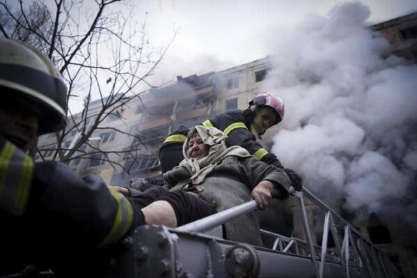 In this photo released by Ukrainian State Emergency Service press service, firefighters evacuate an elderly woman from an apartment building hit by shelling in Kyiv, Ukraine, Monday, March 14, 2022. (Ukrainian State Emergency Service via AP)