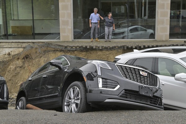 From left, car dealership owner Rick Durand Owner of Durand Cadillac and controller Michelle Bettez react beside three vehicles that fell into a sinkhole that was washed out of his car dealership Tuesday, Sept. 12, 2023, in Leominster, Mass. after more than 9 inches of rain fell overnight. (AP Photo/Josh Reynolds)