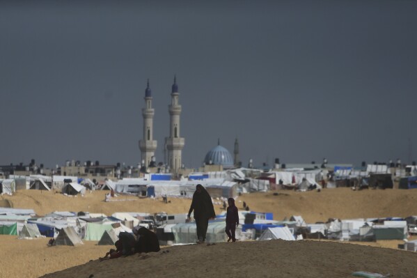 Palestinians displaced by the Israeli ground offensive on the Gaza Strip walk at the makeshift tent camp in Rafah, Gaza Strip, Sunday, Feb. 18, 2024. (AP Photo/Mohammed Dahman)
