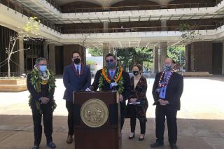 Hawaii Senate President Ron Kouchi speaks at a podium at the state Capitol in Honolulu on Thursday, April 29, 2021, flanked from left to right by Sens. Kalani English, Jarrett Keohokalole, Michelle Kidani and Brian Taniguchi. Hawaii's lawmakers are wrapping up a legislative session marked by a generous influx of federal aid that helped the islands weather the shock of the coronavirus pandemic. (AP Photo/Audrey McAvoy)