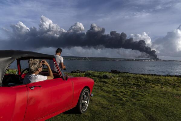 People watch a plume of smoke rise from the Matanzas supertanker base where a deadly fire started during a thunderstorm the night before in Matanzas, Cuba, Sunday, Aug. 7, 2022. The blaze forced officials to evacuate more than 4,900 people, has killed two firefighters, injured 130 people and destroyed four of the facility's eight tanks. (AP Photo/Ramon Espinosa)