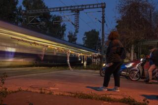 People wait at a rail crossing as a train passes, in Tavros, suburb of Athens, Wednesday, March 22, 2023. Train services have partially resumed in Greece for the first time since a deadly rail disaster three weeks ago, as the country's center-right government struggles to regain its footing ahead of a general election. (AP Photo/Petros Giannakouris)