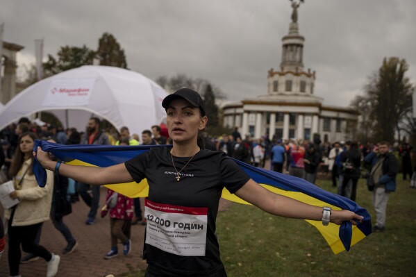 A woman carries the Ukrainian flag after participating in a one-kilometer race in Kyiv, Ukraine, Sunday, Oct. 29, 2023. Around two thousand Ukrainians registered for the event, called 'The World's Longest Marathon', with the dual purpose of honoring the country's military and raising funds to bolster Ukraine's air defense system. (AP Photo/Bram Janssen)