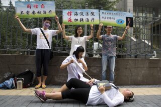 FILE - In this July 31, 2014 file photo, gay rights campaigners act out electric shock treatment to protest outside a court when the first court case in China involving so-called conversion therapy is held in Beijing, China. A gay man in central China has successfully sued a mental hospital over forced conversion therapy on June 26, 2017, in what activists are hailing as the first such victory in the country where the LGBT rights movement is gradually emerging form the fringes. (AP Photo/Ng Han Guan, File)