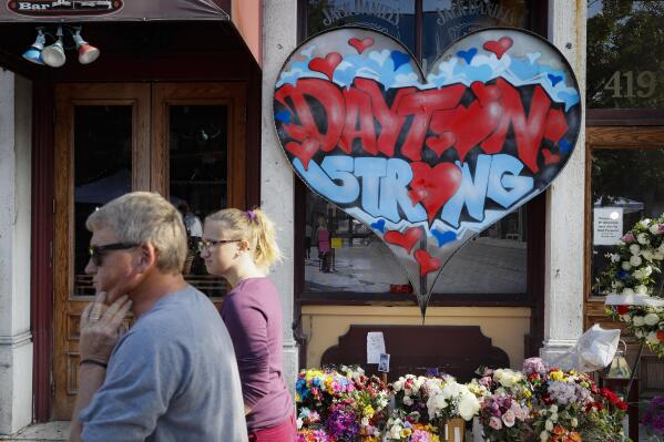 FILE - In this Aug. 7, 2019 file photo, pedestrians pass a makeshift memorial for the slain and injured victims of a mass shooting that occurred in the Oregon District in Dayton, Ohio. Relatives of four people killed when a gunman opened fire two years ago have sued the maker of a high-capacity magazine used by the shooter. The lawsuit against Nevada-based Kyung Chang Industry USA Inc. alleges negligence, negligent entrustment, and public nuisance by the company. The lawsuit filed in Nevada o n Sunday, Aug. 1, 2021 says high-capacity magazines have only one purpose: to kill multiple people as quickly as possible. (AP Photo/John Minchillo, File)