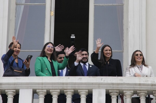 Congresswoman Nydia Velazquez, (D-NY), from left, Santiago's Mayor Iraci Hassler, Congressman Maxwell Frost, (D-FL), Congressman Greg Casar, (D-TX), Congresswoman Alexandria Ocasio-Cortez, (D-NY), and Misty Rebik, chief of Staff for Sen. Bernie Sanders, wave to students from a City Hall balcony, in Santiago, Chile, Thursday, Aug. 17, 2023. The US delegation traveled to the South American country to learn about efforts to defend its democracy ahead of the 50th anniversary of the military coup led by Gen. Augusto Pinochet. (AP Photo/Esteban Felix)