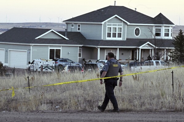 FILE - A sheriff's deputy from the El Paso County Sheriff's Department walks down the road after reattaching crime scene tape across the road that leads to a house, Dec. 7, 2023, in Peyton, Colo. On Tuesday, Dec. 12, Colorado authorities released the identities of four people, including three family members, who were found dead inside the home in rural Colorado following a reported shooting the week before. (Jerilee Bennett/The Gazette via AP, File)