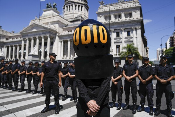 A demonstrator wearing the Spanish word "Hate" stands in front of police standing guard outside Congress as protesters rally during a national strike against the economic and labor reforms proposed by Argentine President Javier Milei in Buenos Aires, Argentina, Wednesday, Jan. 24, 2024. (AP Photo/Rodrigo Abd)