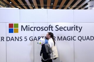FILE - A woman walks in front of the Microsoft stand during the Cybersecurity Conference in Lille, northern France, Wednesday Jan. 29, 2020. Microsoft announced legal action Monday, Oct. 12, 2020 seeking to disrupt a major cybercrime digital network that uses more than 1 million zombie computers to loot bank accounts and spread ransomware, which experts consider a major threat to the U.S. presidential election. (AP Photo/Michel Spingler)