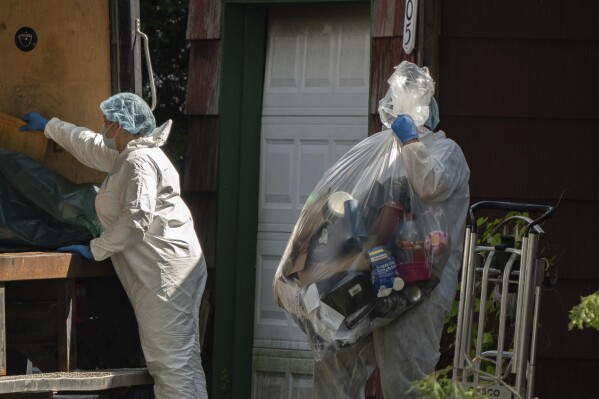 A crime laboratory officer moves a plastic bag of items as law enforcement searches the home of Rex Heuermann, Saturday, July 15, 2023, in Massapequa Park, N.Y. Heuermann, a Long Island architect, was charged Friday, July 14, with murder in the deaths of three of the 11 victims in a long-unsolved string of killings known as the Gilgo Beach murders. (AP Photo/Jeenah Moon)