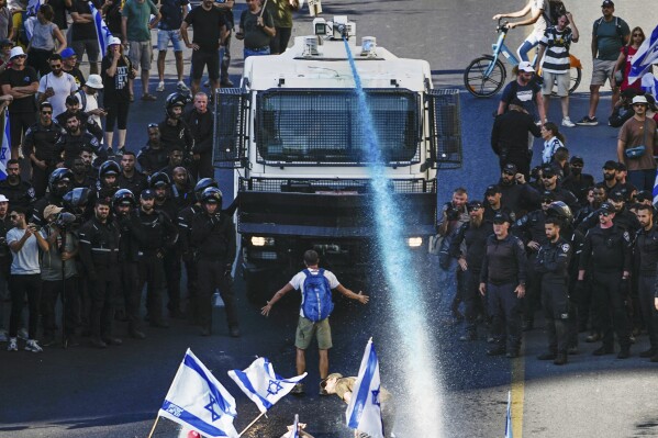 A person stands in front of an Israeli police water cannon being used to disperse demonstrators blocking a road during a protest against plans by Prime Minister Benjamin Netanyahu's government to overhaul the judicial system, in Jerusalem, Monday, July 24, 2023. Israeli lawmakers on Monday approved a key portion of Prime Minister Benjamin Netanyahu's divisive plan to reshape the country's justice system despite massive protests that have exposed unprecedented fissures in Israeli society. (AP Photo/Ariel Schalit)