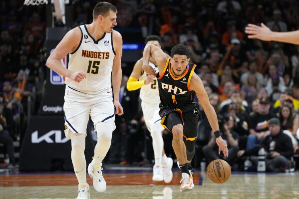 Phoenix Suns guard Devin Booker (1) drives as Denver Nuggets center Nikola Jokic (15) looks on during the first half of Game 4 of an NBA basketball Western Conference semifinal game, Sunday, May 7, 2023, in Phoenix. (AP Photo/Matt York)