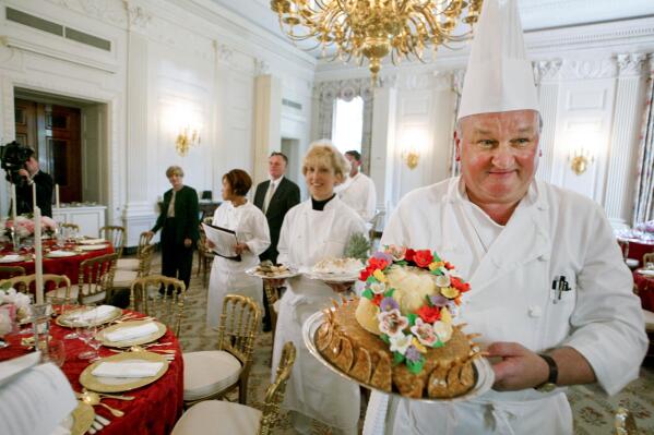 FILE - White House pastry chef Roland Mesnier, right, displays a mango coconut lei, the dessert for the dinner hosted by President George W. Bush for Philippine President Gloria Macapagal Arroyo, in the State Dining Room in the White House in Washington, May 19, 2003. Mesnier, a White House executive chef and who served five presidential administrations for roughly 25 years, died Friday, Aug. 26, 2022. (AP Photo/Charles Dharapak, File)