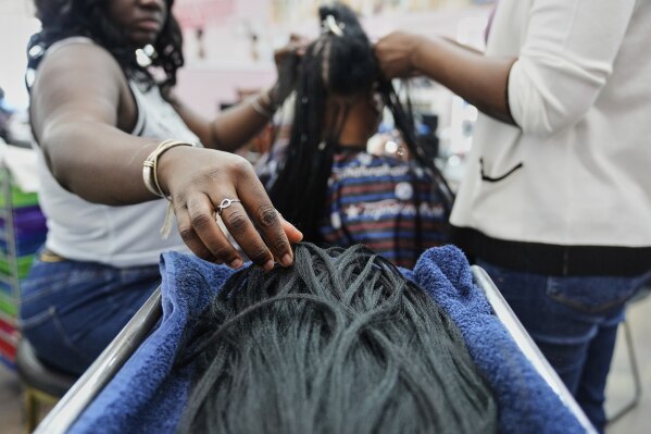 A braider at Eve's African Braiding in College Park, Ga., picks up pieces of synthetic braiding hair to feed into client Sadajah Herring's hair to create knotless braids, Tuesday, May 6, 2025. (AP Photo/Stephanie Scarbrough)