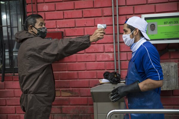 A security guard takes a worker's temperature at the entrance of a fish market in the Villa Maria del Triunfo district on the outskirts of Lima, Peru, Wednesday, May 27, 2020, amid the new coronavirus pandemic. (AP Photo/Rodrigo Abd)