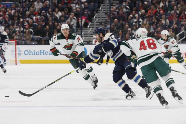 Columbus Blue Jackets' Boone Jenner, center, carries the puck across the blue line between Minnesota Wild's Joel Eriksson Ek, left, and Jared Spurgeon during the second period of an NHL hockey game Friday, March 11, 2022, in Columbus, Ohio. (AP Photo/Jay LaPrete)