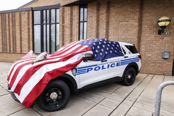 An American flag and flowers cover a Charlotte-Mecklenburg police vehicle at the North Tryon Station in Charlotte, N.C., Tuesday, April 30, 2024 where Charlotte-Mecklenburg Officer Joshua Eyer was stationed. Police in North Carolina say a shootout that killed four law enforcement officers, including Eyer, and wounded four others began as officers approached the home to serve a warrant for a felon wanted for possessing a firearm on April 29. (AP Photo/Nell Redmond)