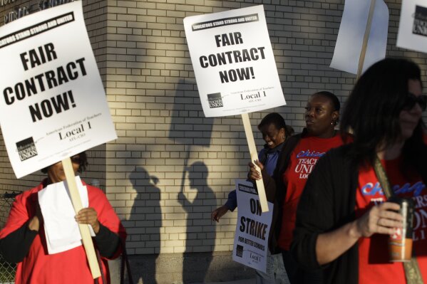 FILE - This Sept. 10, 2012 file photo shows Chicago teachers walk walking a picket line outside a school in Chicago. A threatened strike in 2019 by Chicago teachers would carry on the city's historically significant role in education labor disputes, including the 2012 strike cited by teachers around the country as inspiration for walkouts and other protests in recent years. That seven-day strike was a dramatic test of the Chicago Teachers Union's effort to force expanded negotiations into social issues beyond the typical give-and-take over pay and benefitsAP Photo/M. Spencer Green, File)