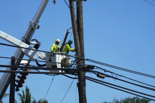 FILE - Linemen work on poles Aug. 13, 2023, in Lahaina, Hawaii, following a deadly wildfire that caused heavy damage days earlier. When the winds of Hurricane Dora lashed Maui Aug. 8, they struck bare electrical lines the Hawaiian electric utility had left exposed to the elements. (AP Photo/Rick Bowmer, File)