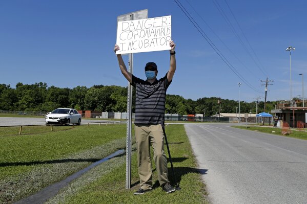 Protestor Trey Bennett holds a sign towards members of the Life Tabernacle Church waiting outside the East Baton Rouge Parish jail for Pastor Tony Spell to post bond in Baton Rouge, La., Tuesday, April 21, 2020. Louisiana authorities arrested the pastor on an assault charge on Tuesday after he admitted that he drove his church bus toward Bennett, who has been protesting Spell's decision to hold mass gatherings in defiance of public health orders during the coronavirus pandemic. (AP Photo/Gerald Herbert)