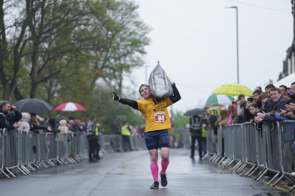 Brett Spencer gestures to the crowd as he makes his way to the finish line carrying a 50kg sack of coal during the World Coal Carrying Championships in Ossett, West Yorkshire, England, Monday, April 21, 2025. (AP Photo/Jon Super)